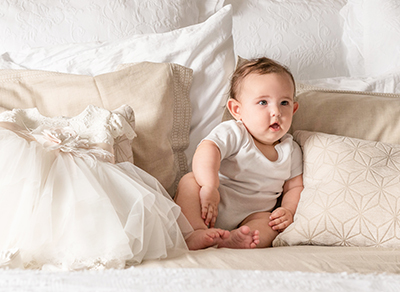 Baby girl sitting propped up by pillows on a bed