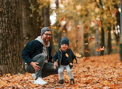 Father and child playing with leaves in an autumn forest