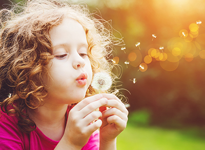 Girl lit up in golden light blowing dandellion