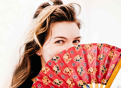 Portrait of girl with a sly smile looking over a fan